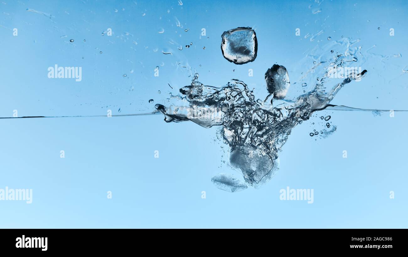 transparent water with falling ice cubes and splash on blue background ...