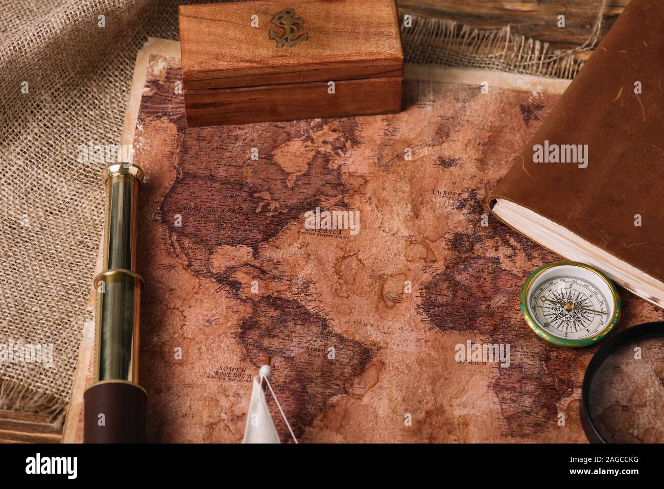 wooden box, telescope, compass and aged world map on hessian Stock