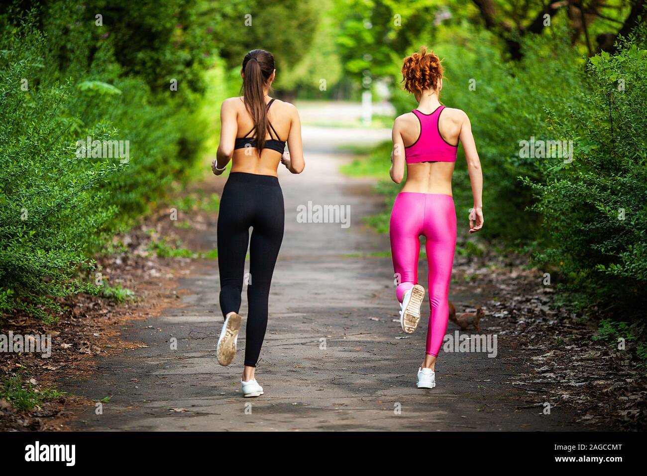 Fitness. Two female runners stretching legs outdoors in park in summer