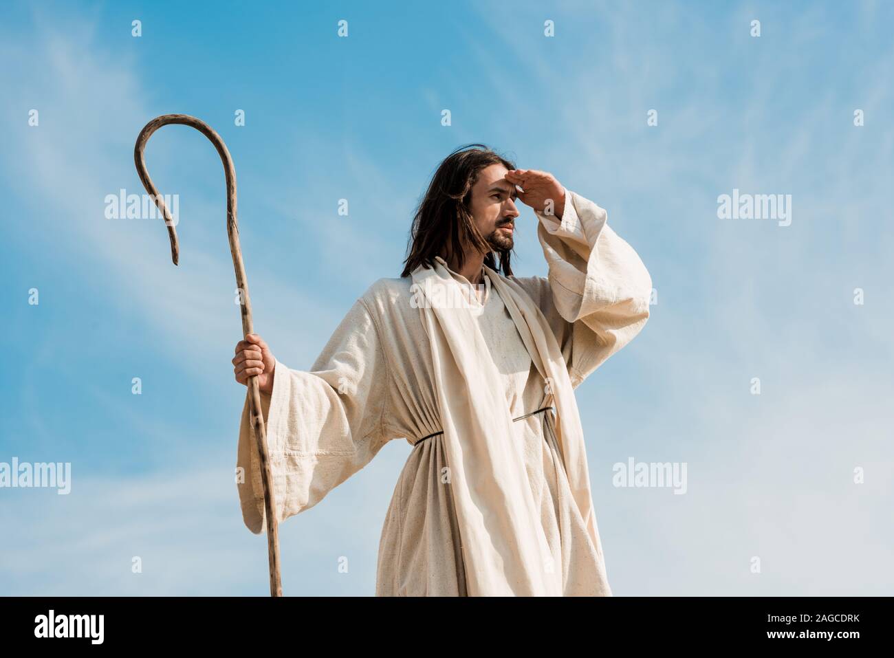 bearded man holding wooden cane against blue sky and clouds Stock Photo