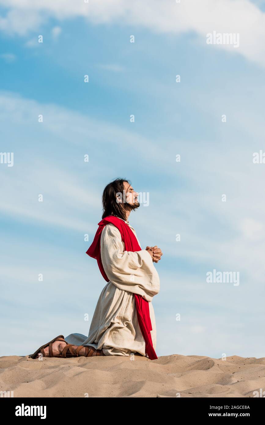 Jesus in robe, red sash and crown of thorns holding rosary and praying with  closed eyes in desert Stock Photo by LightFieldStudios