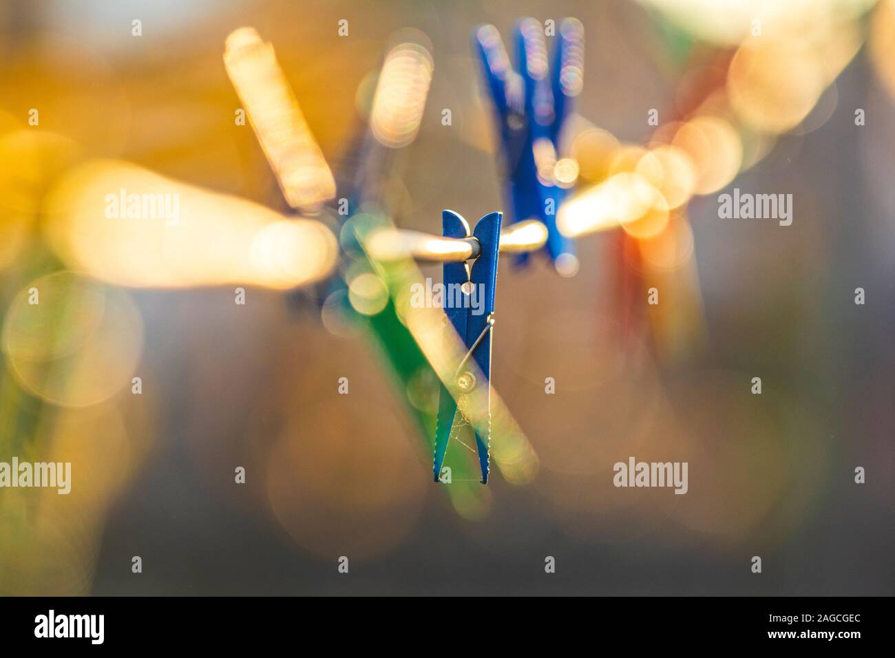 Colorful clips for washing laundry on strip rope outdoor. Sunset light, backlight, golden bokeh. Winter autumn housework concept, close up, shallow de Stock Photo