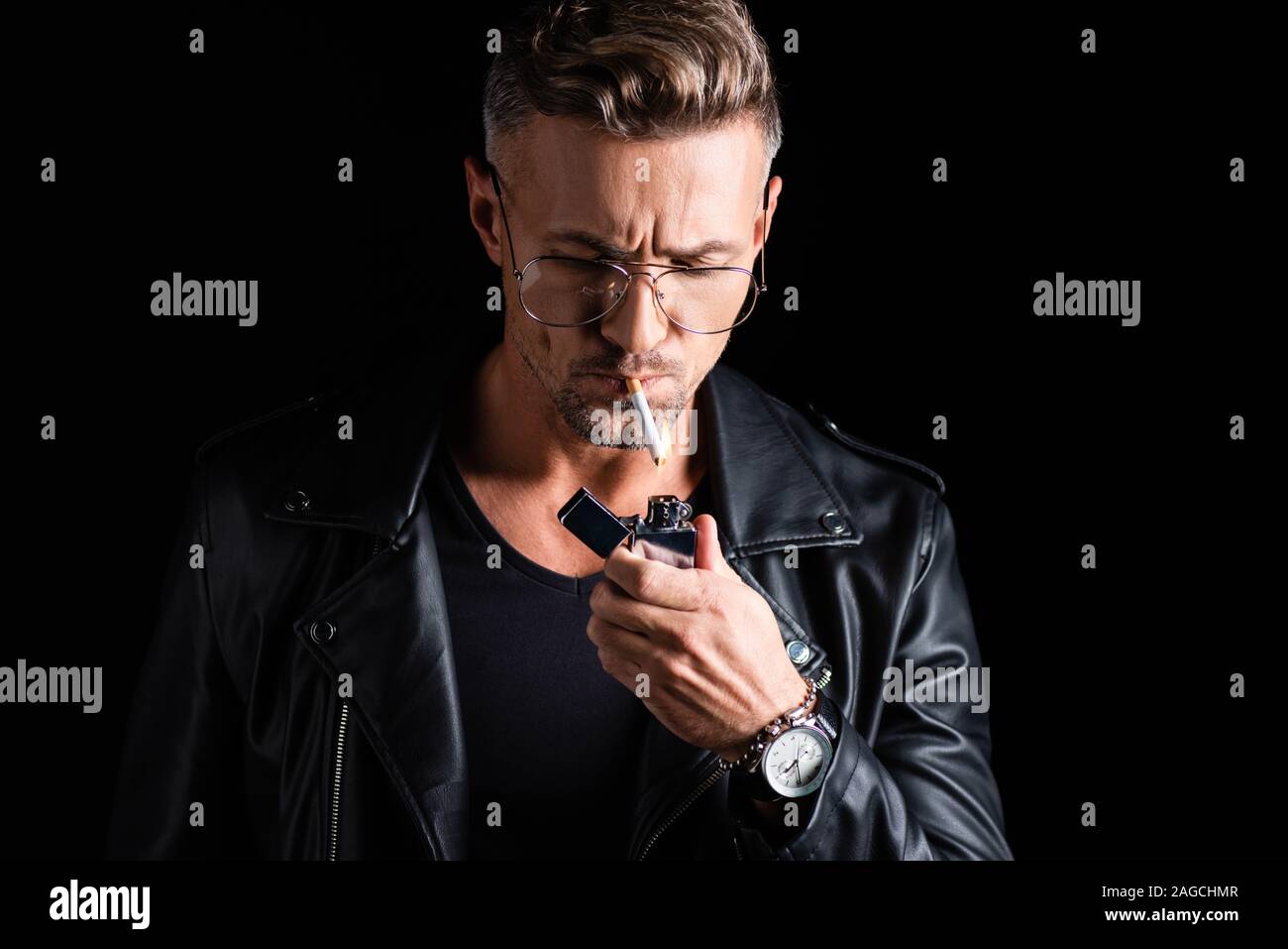 Handsome man in leather jacket lighting cigarette with lighter isolated on black Stock Photo