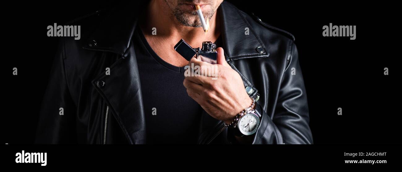 Cropped view of man in leather jacket lighting cigarette with lighter isolated on black, panoramic shot Stock Photo