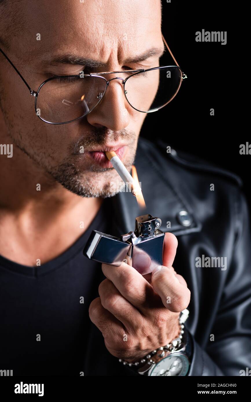 Handsome man in sunglasses lighting cigarette with lighter isolated on black Stock Photo