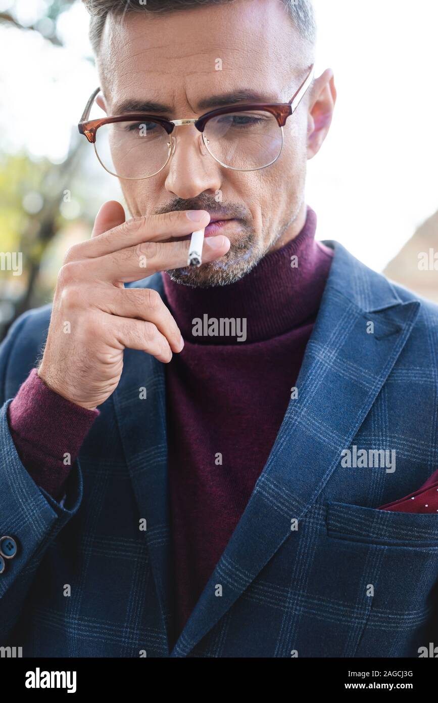 businessman smoking cigarette Handsome businessman smoking cigarette and looking down outdoors Stock  Photo