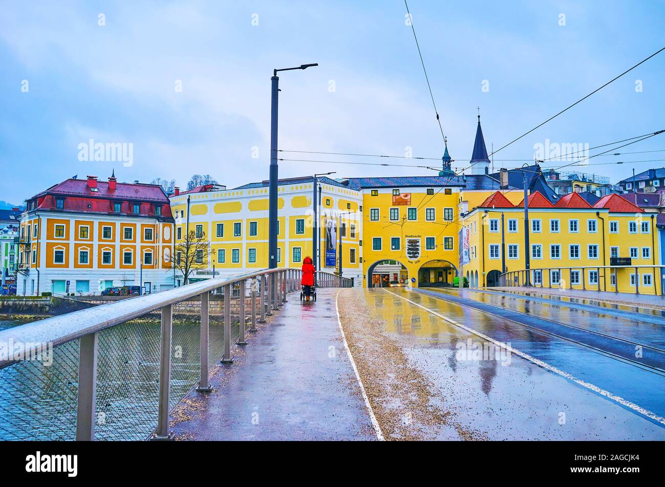 GMUNDEN, AUSTRIA - FEBRUARY 22, 2019: The rainy day in Gmunden with reflections of old town's buildings on the dark road of wet Traun bridge (Traunbru Stock Photo