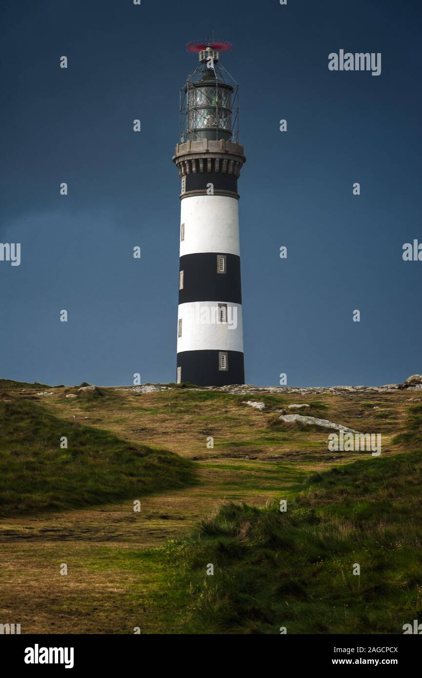 Vertical low angle shot of a lighthouse under the dark sky in a grassy ...