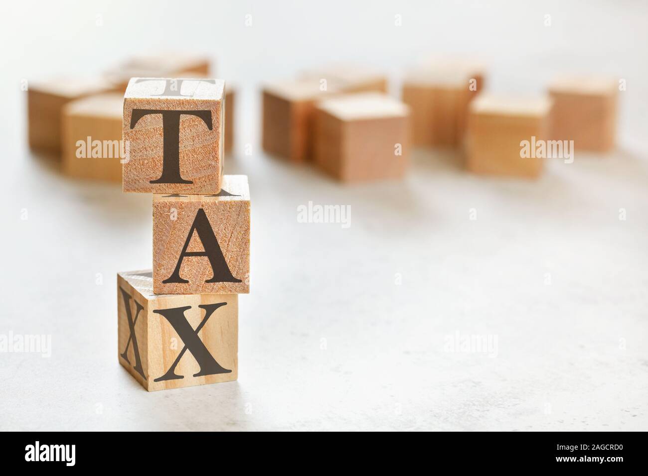 Three wooden cubes with word TAX on white table, more in background, space for text in right down corner Stock Photo