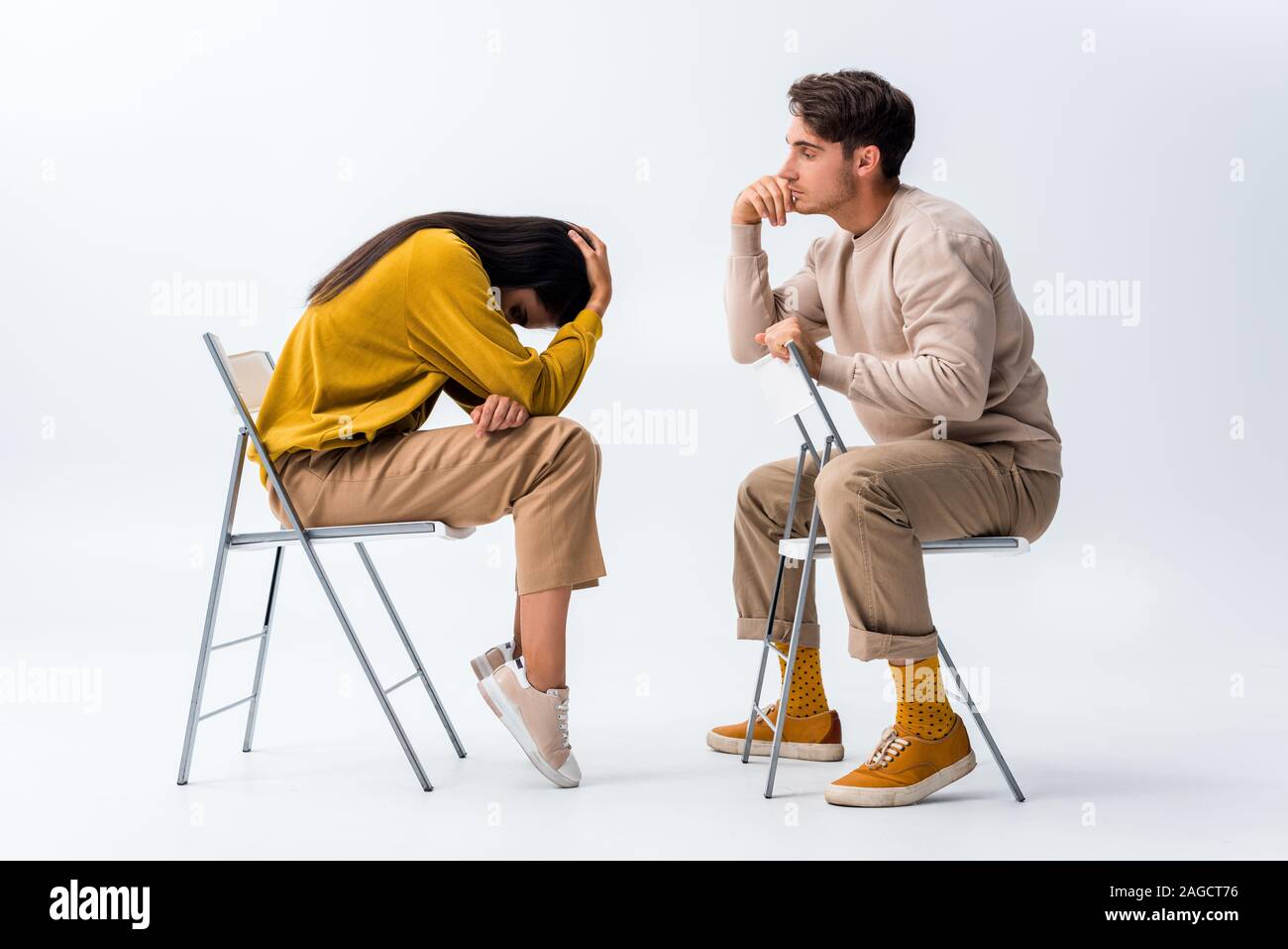 man sitting on chair and looking at upset woman covering face on white Stock Photo