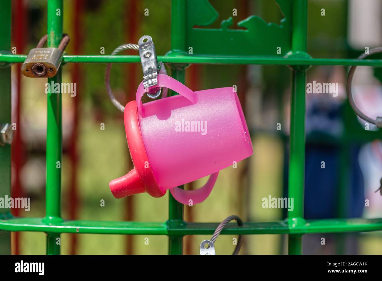 pink baby drinking cup clipped to a lost item rack in a park Stock Photo