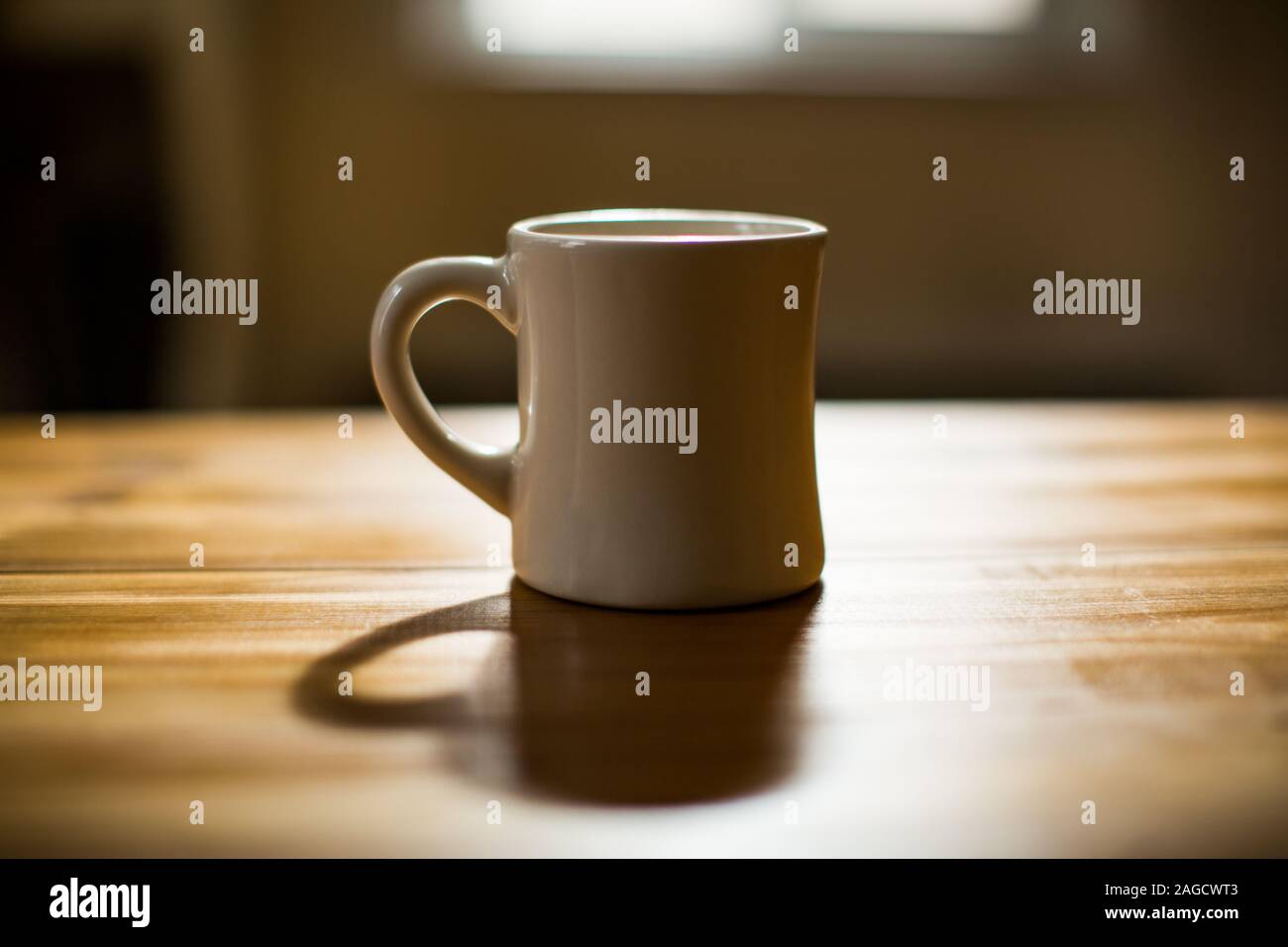 White mug on a brown wooden table with a blurred background Stock Photo