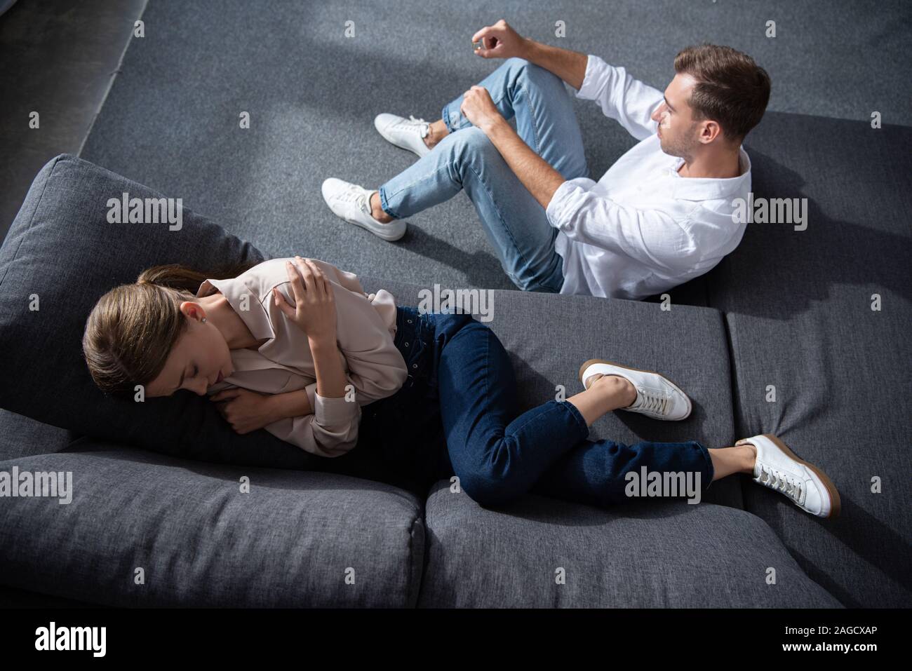 overhead view of crying woman lying on sofa and man sitting on floor Stock Photo