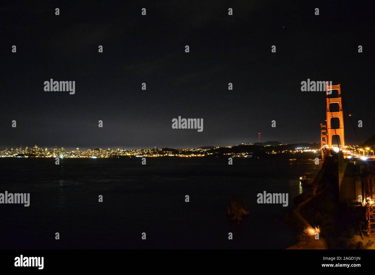 Golden Gate Bridge in the night with the city lights reflecting on the water in the background Stock Photo