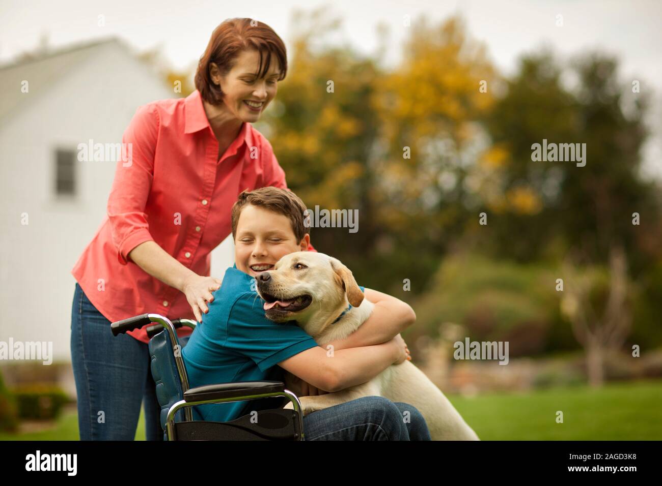 Smiling teenage boy hugging a dog while his mother looks on. Stock Photo