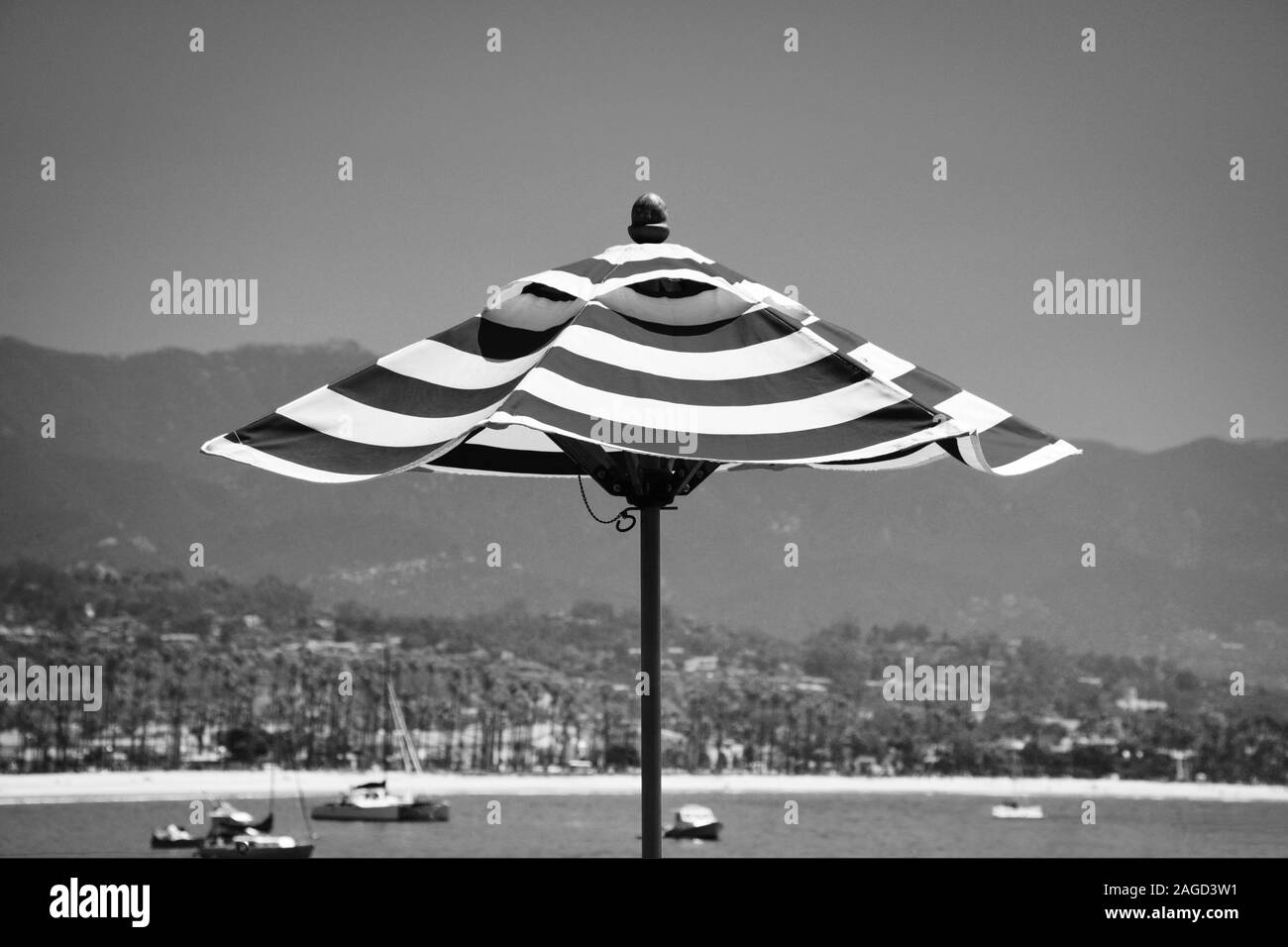 A close up of a striped beach or patio umbrella with a background of sailboats in the Santa Barbara harbor with in black and white, Santa Barbara,  CA Stock Photo