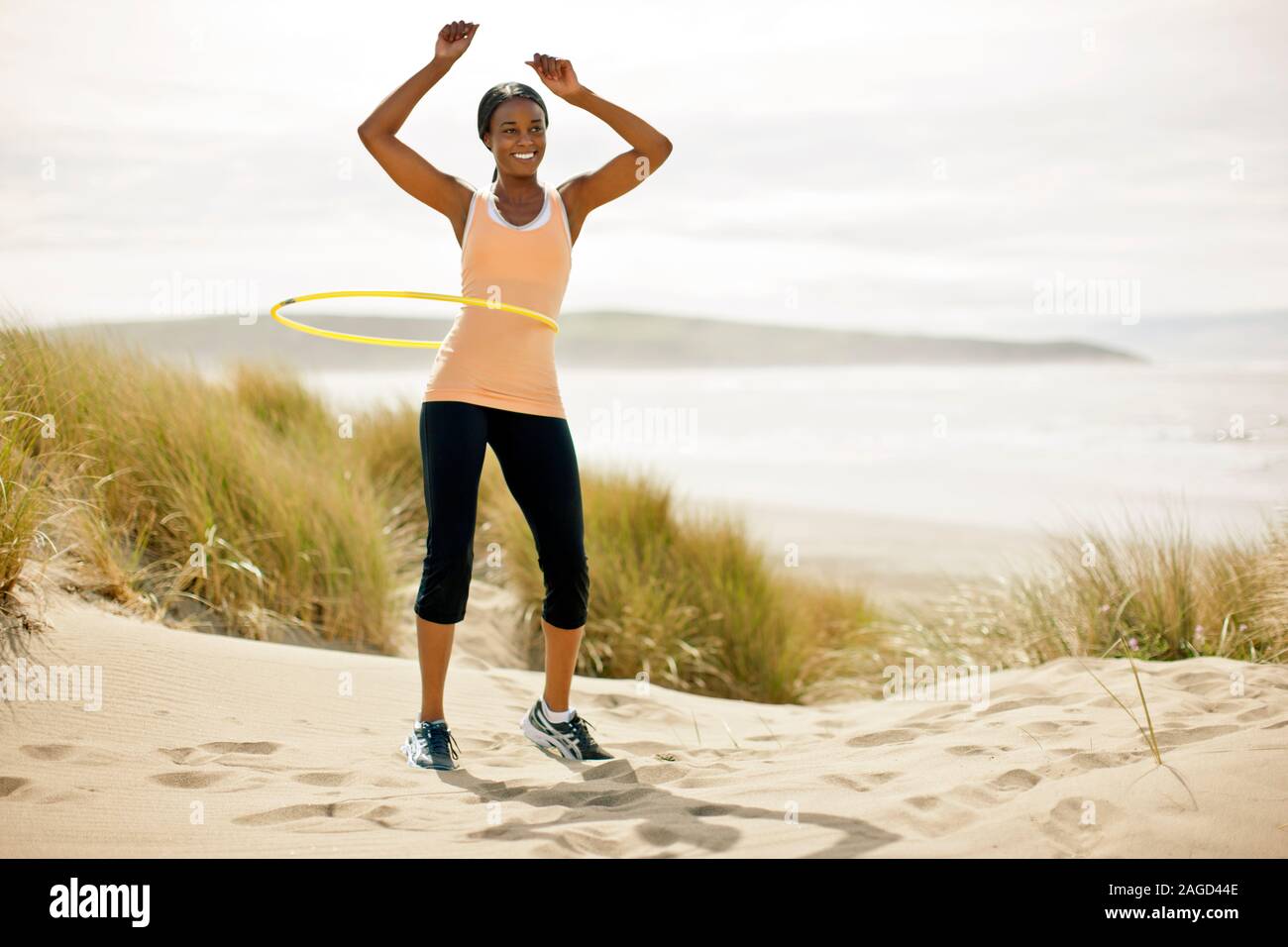 Happy young woman hula hooping on a beach. Stock Photo