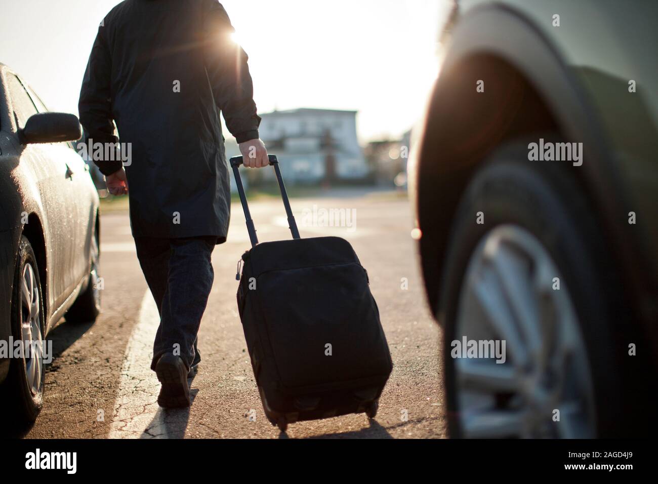 Suitcase on wheels being pulled across a parking lot by a mid adult man. Stock Photo