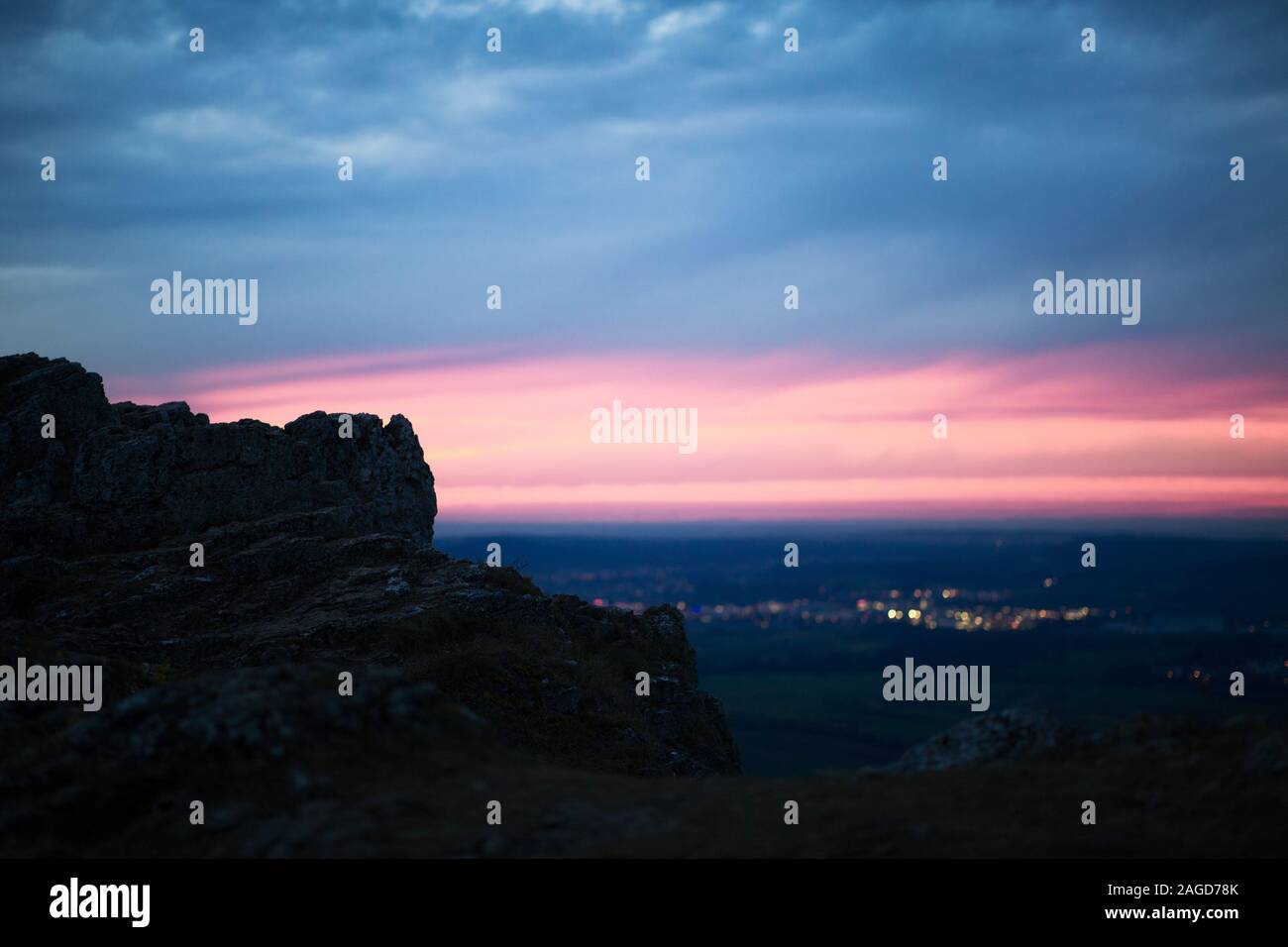 Beautiful view of the city and lights from the rocks under a cloudy sky during the sunset Stock Photo