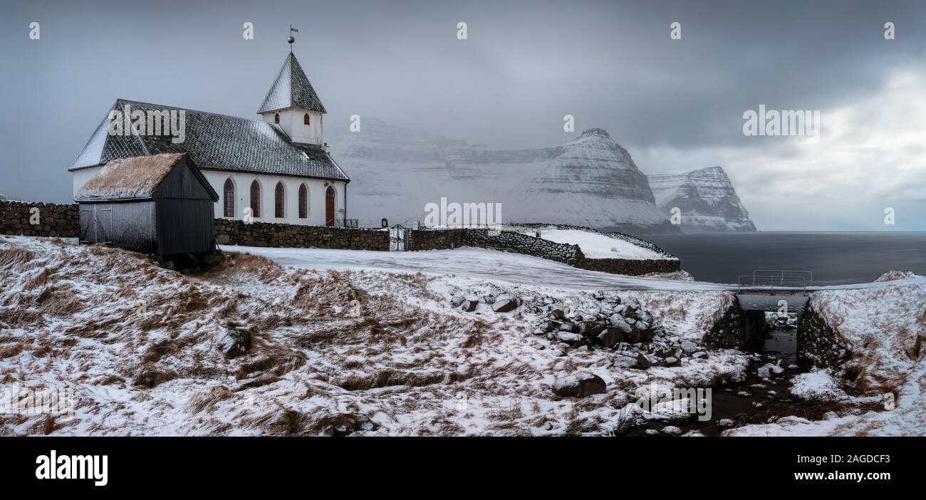 White church in snowy Vidareidi village with Bordoy and Kunoy islands in background, Faroe Islands Stock Photo