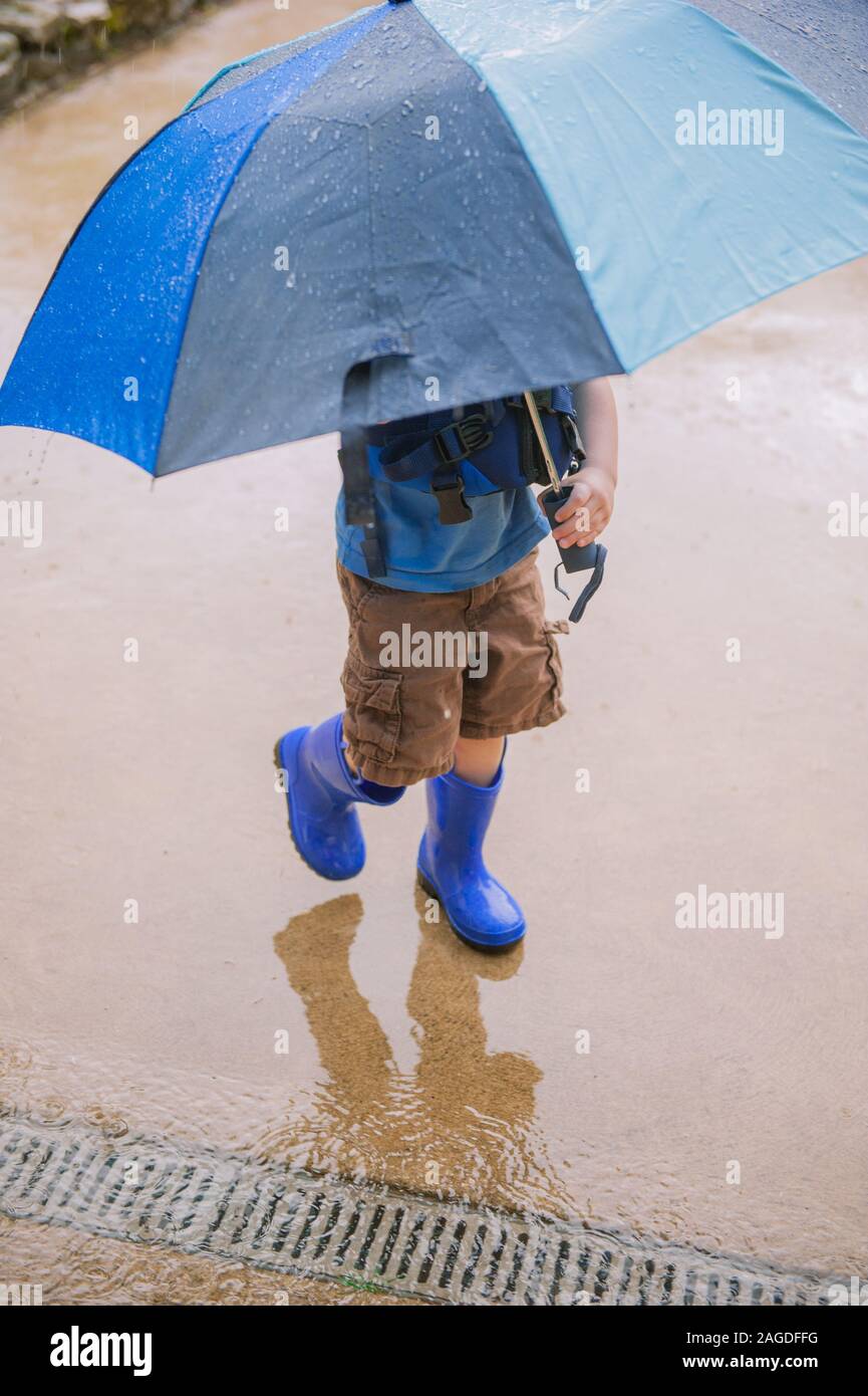 Vertical shot of a little boy with an umbrella and blue rubber boots ...