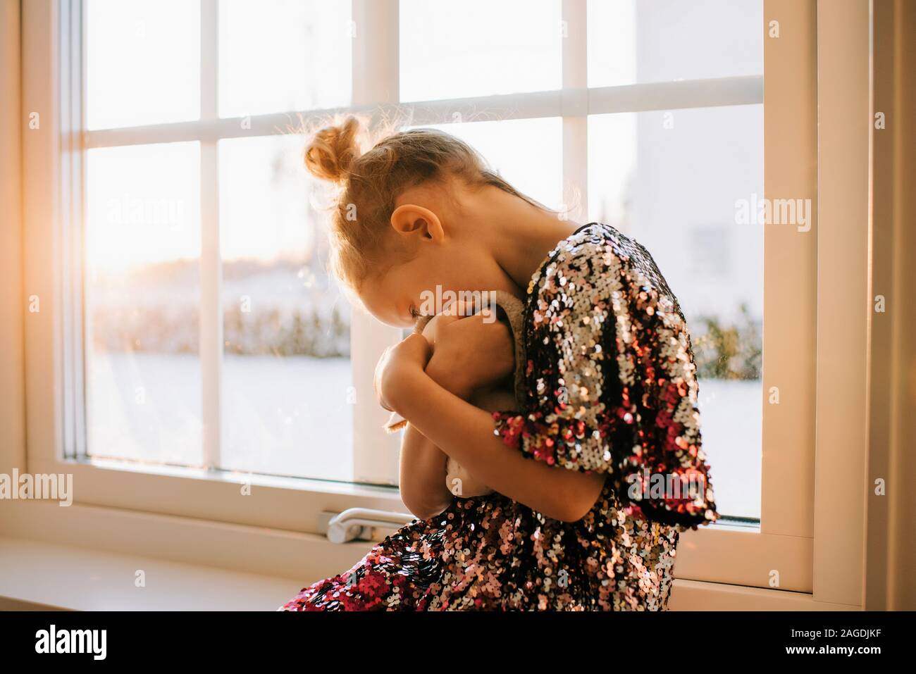 young girl playing with her toy at home in a sparkly dress at sunset Stock Photo