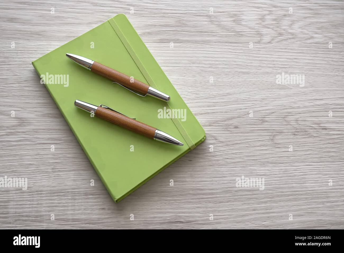 High angle shot of two pens on a green notebook on a wooden surface Stock Photo
