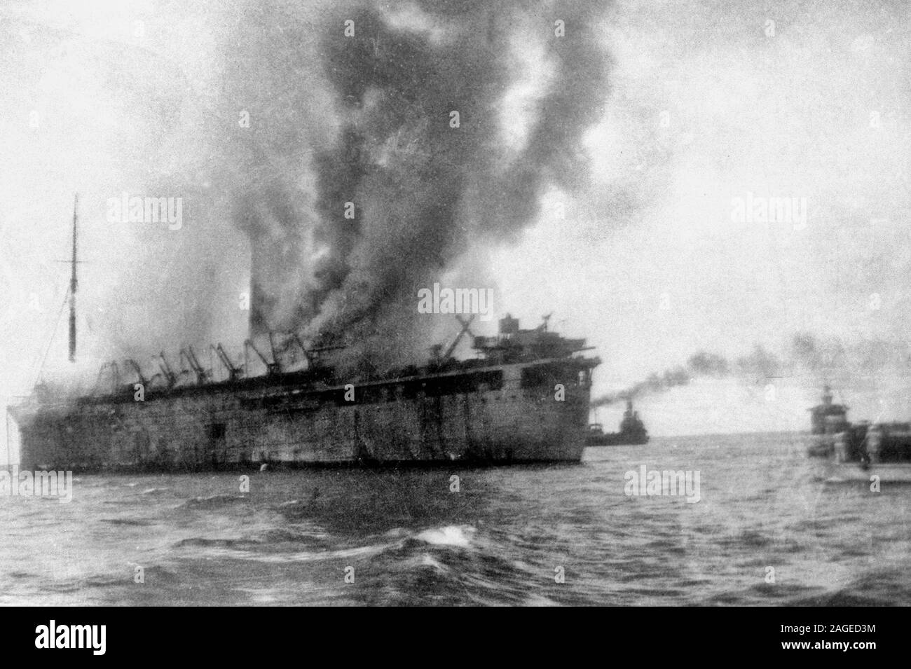 Starboard side view of the extensively damaged British transport the Empress of Asia and Navy rescue vessels. The transport was set on fire during a bomb attack by Japanese aircraft. It was one of four ships bringing the remainder of the 18th British Division, some other troops, and transport vehicles to the island. Most of the troops were rescued by the Navy, but nearly all their weapons and equipment were lost. Singapore, February 1942 Stock Photo