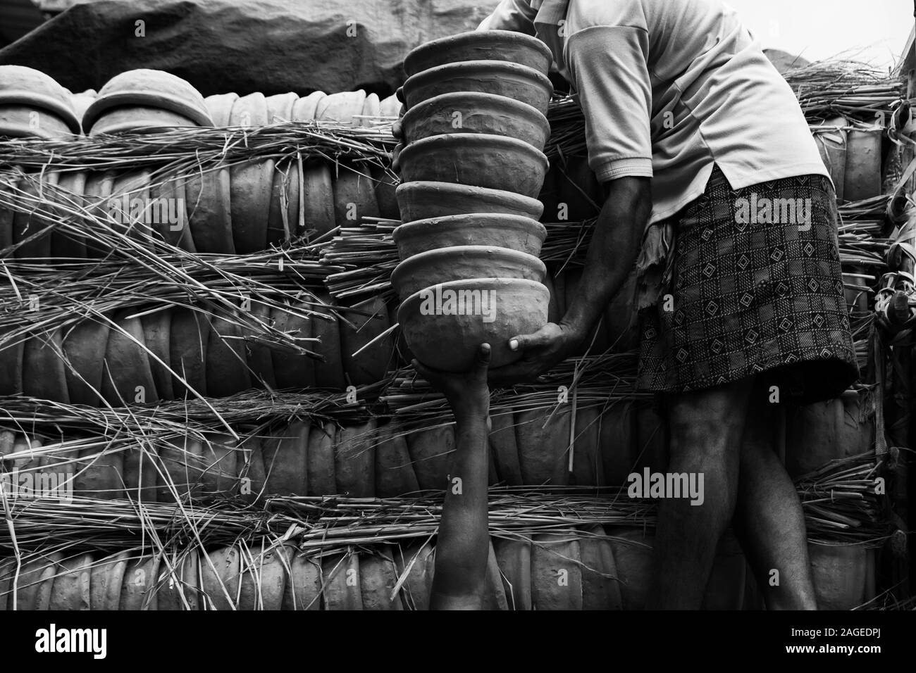 Greyscale of a person holding a stack of clay pots standing near the pots covered with woods Stock Photo