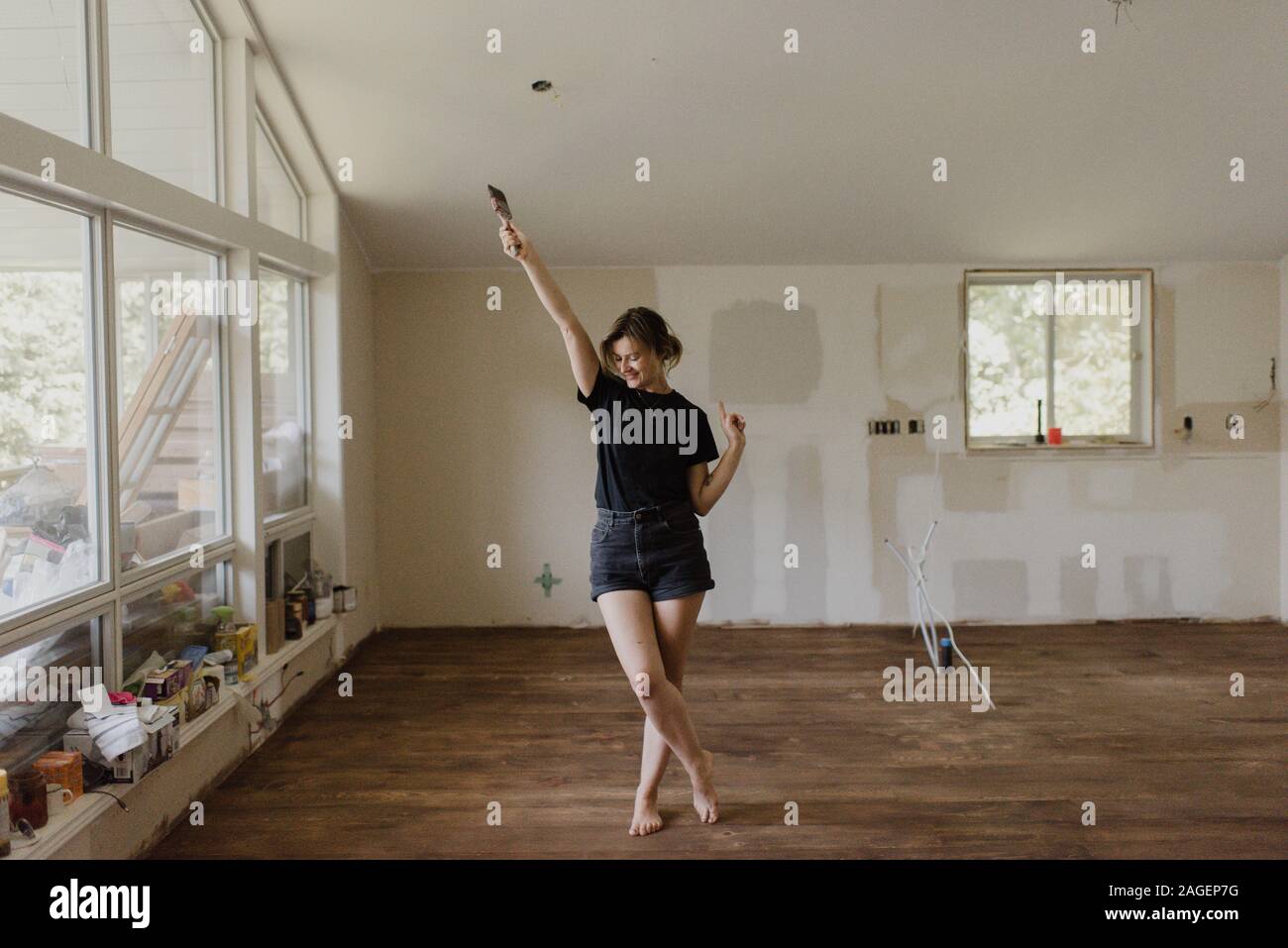 Woman holding paintbrush and dancing in new home Stock Photo