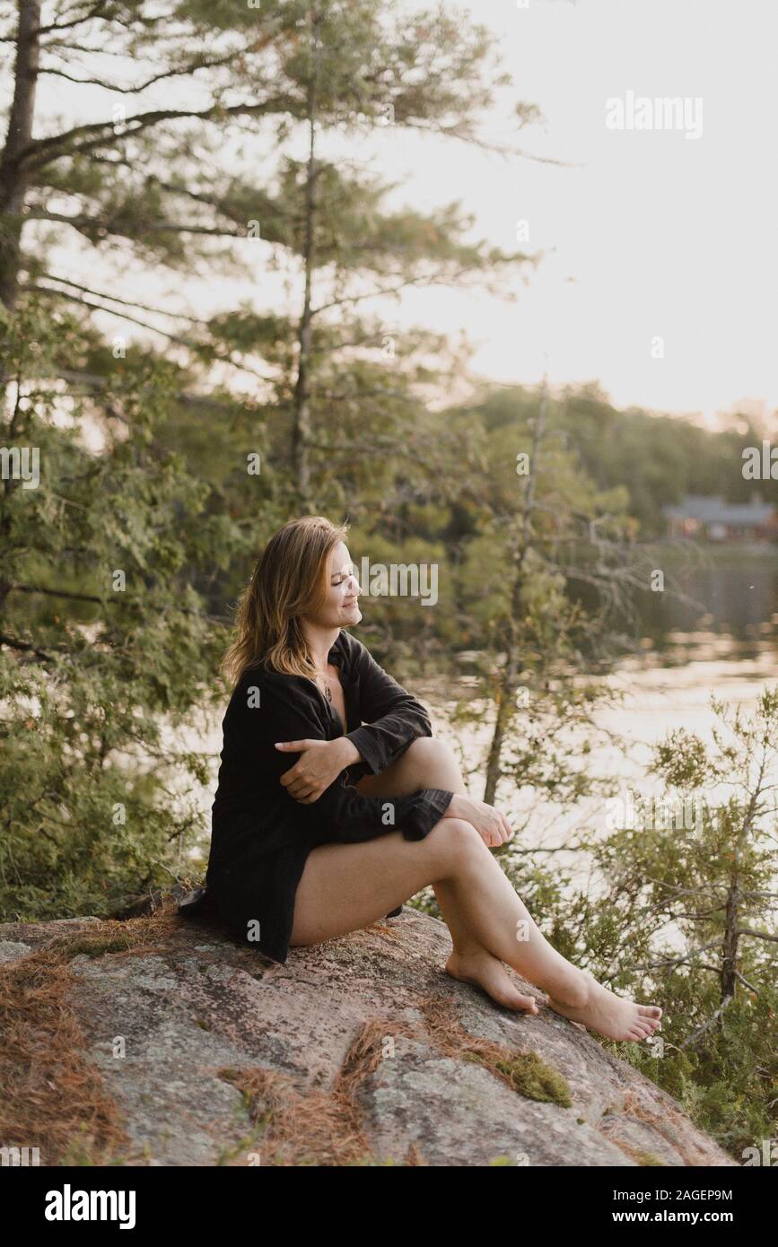 Woman relaxing on boulder by lake, Bobcaygeon, Ontario, Canada Stock Photo