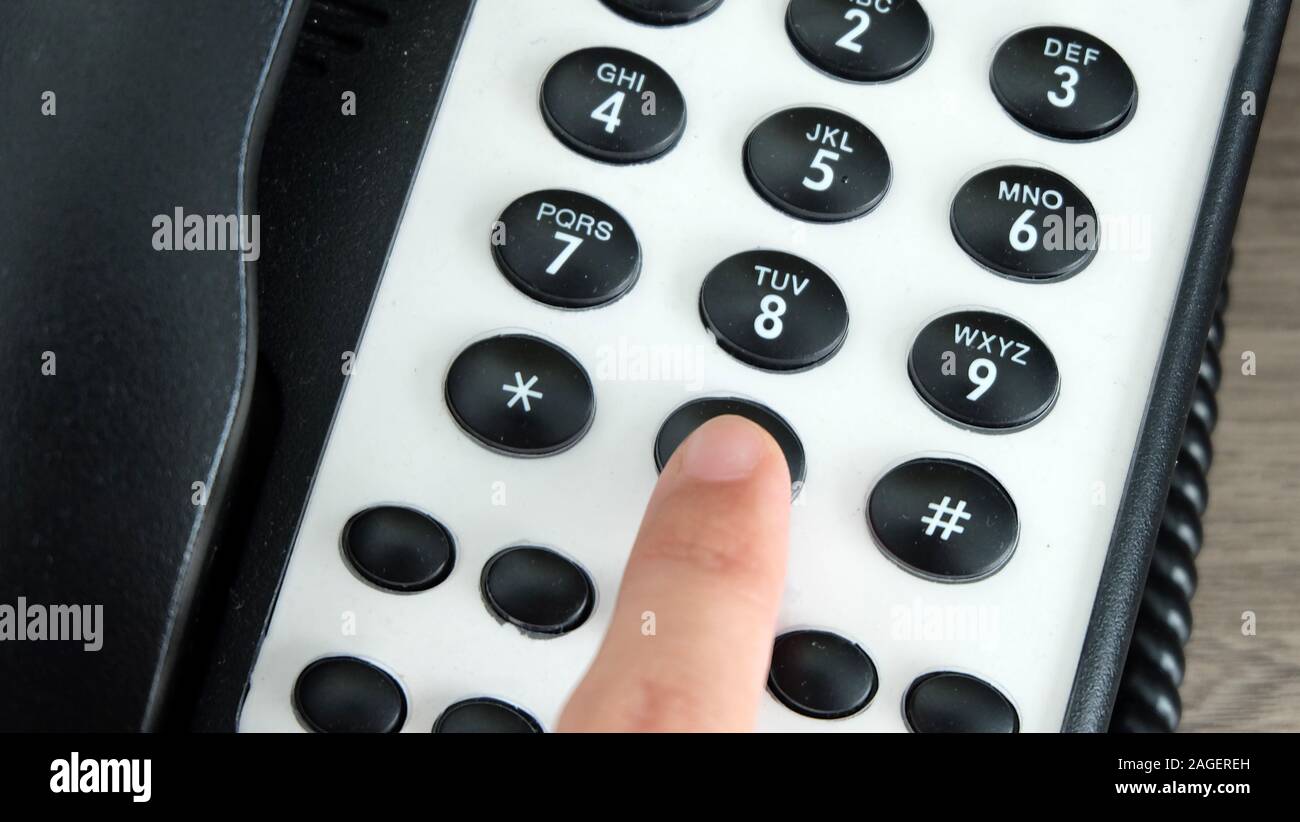 Hand pressing the 0 dial key of an office phone. Stock Photo