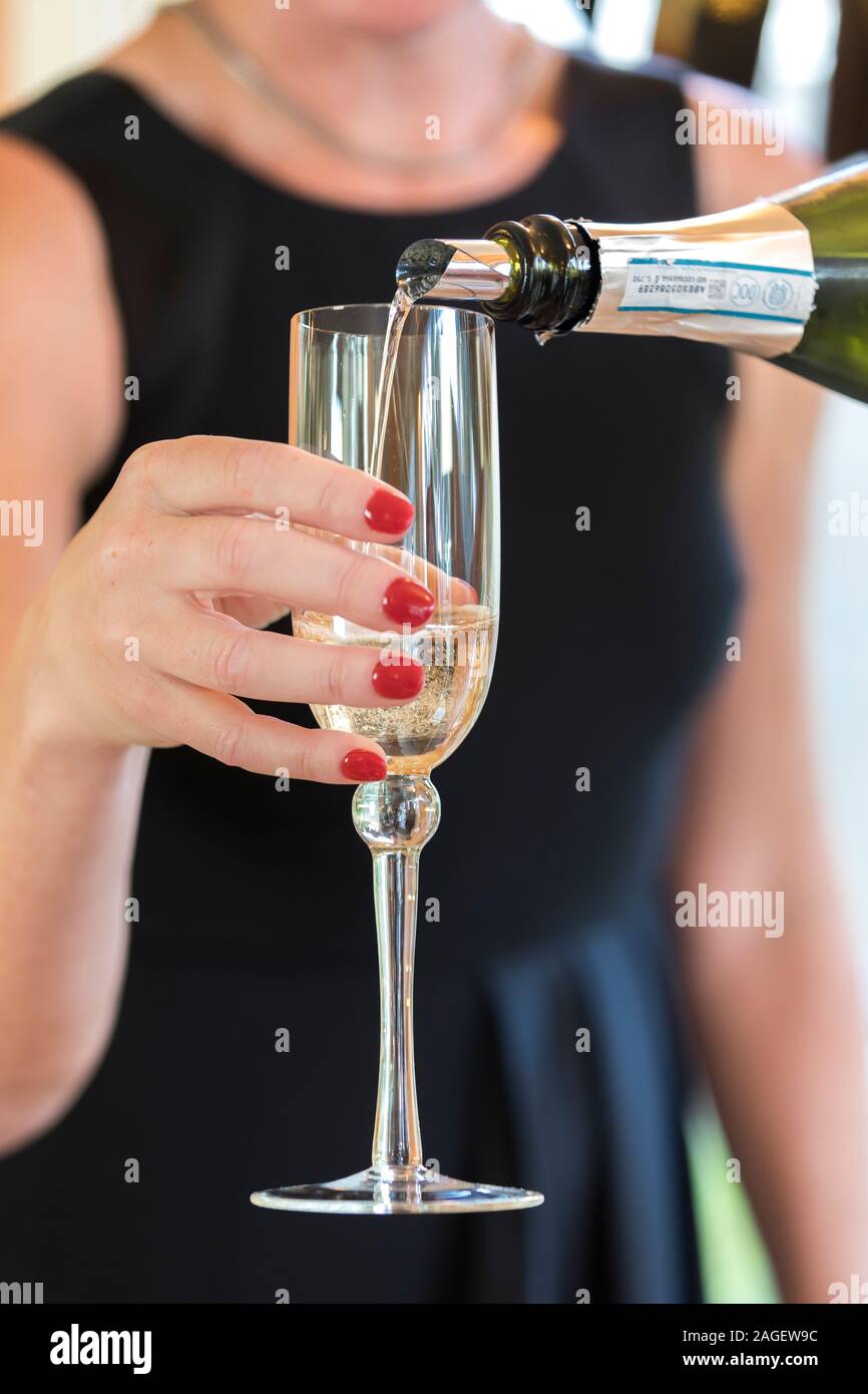 close up of champagne being poured into glass with female hand holding Stock Photo