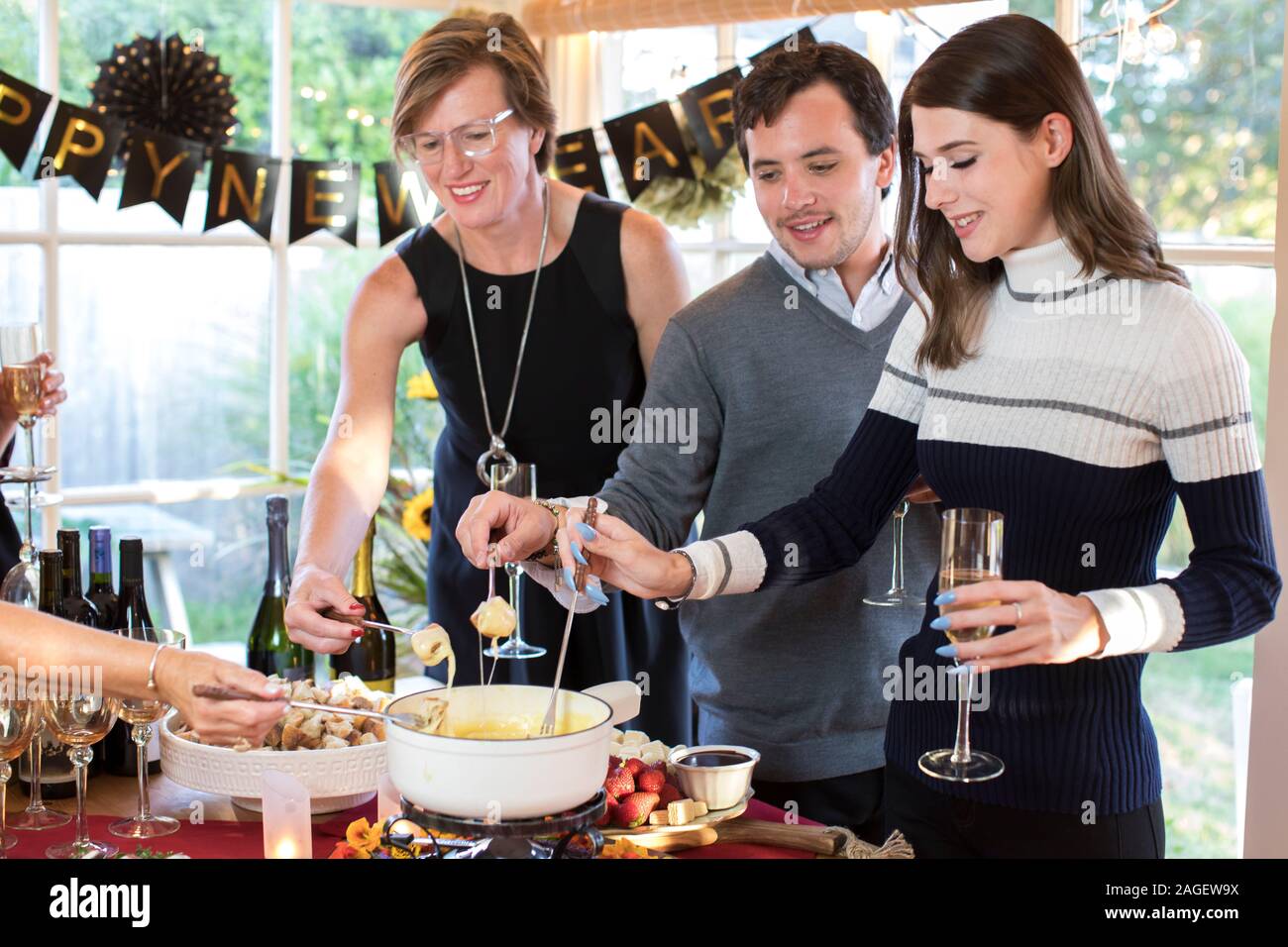 party-goers dipping bread in cheese fondue at a holiday fondue party Stock Photo