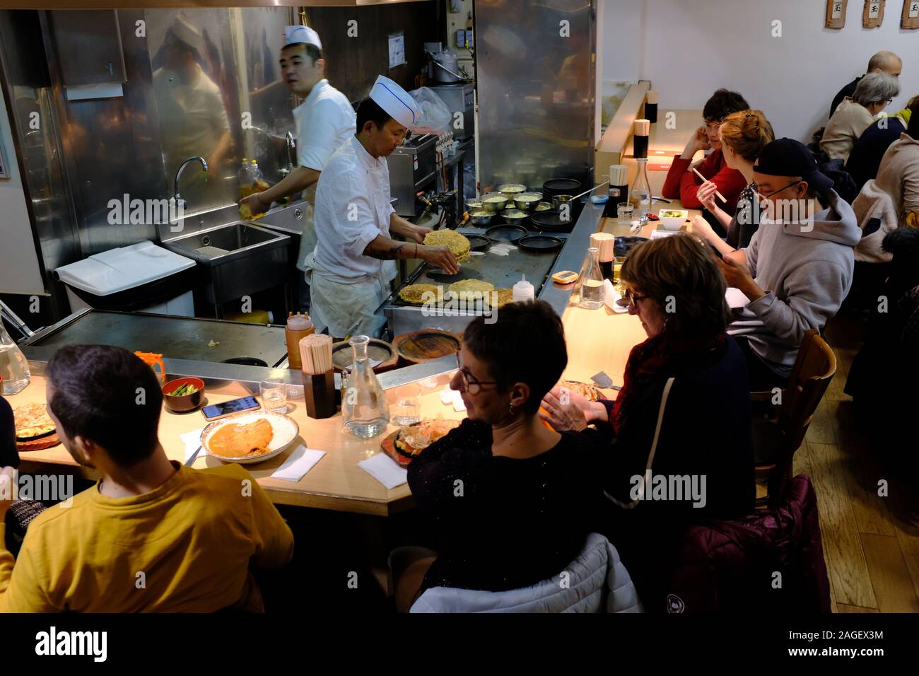 Customers eating at a Japanese restaurant with an open kitchen. Rue