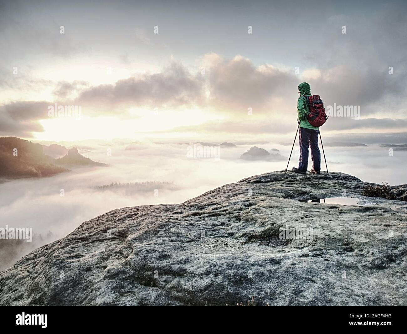 Young woman tourist standing on mountain top and looking to misty nowhere. Girl hiker alone lost in foggy cloud in high mountains. Stock Photo