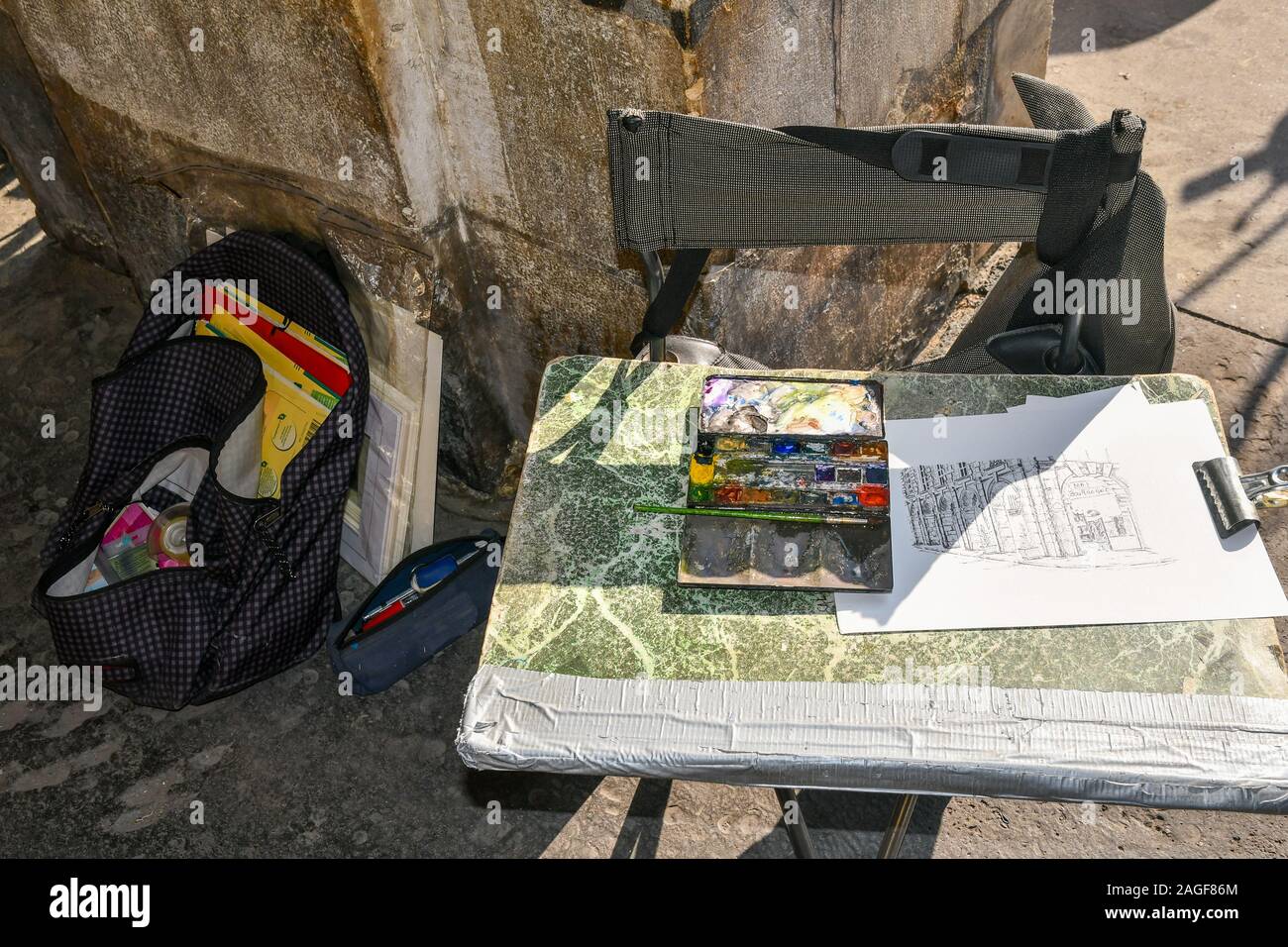 Close-up of street artist tools with a preparatory drawing and watercolors box on a folding chair under the arcade in Place des Vosges, Paris, France Stock Photo
