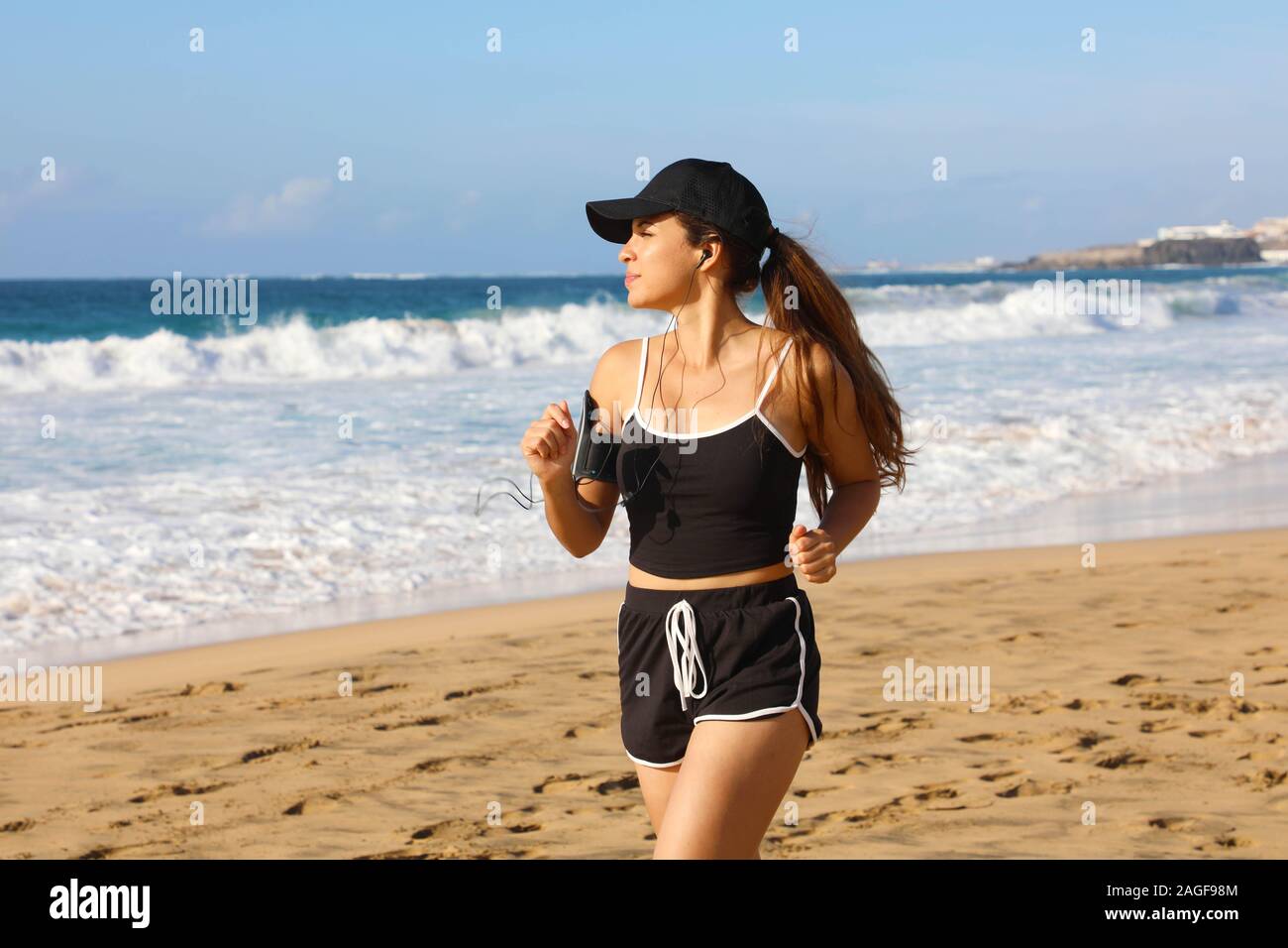 Running woman with listening to on her phone sports armband with touchscreen and earphones on summer beach Stock Photo - Alamy