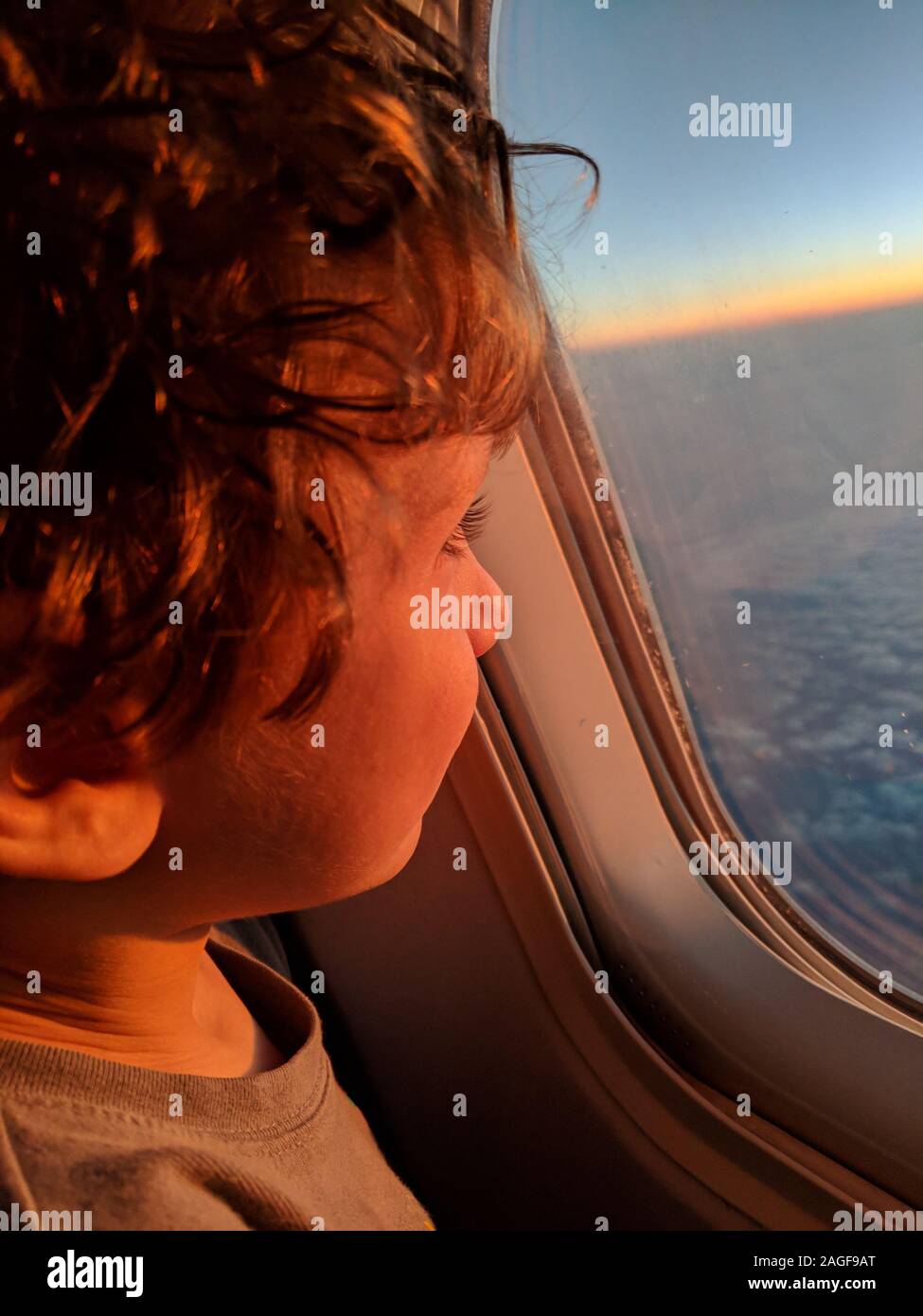 Little boy looking out of a plane window at the sunrise Stock Photo