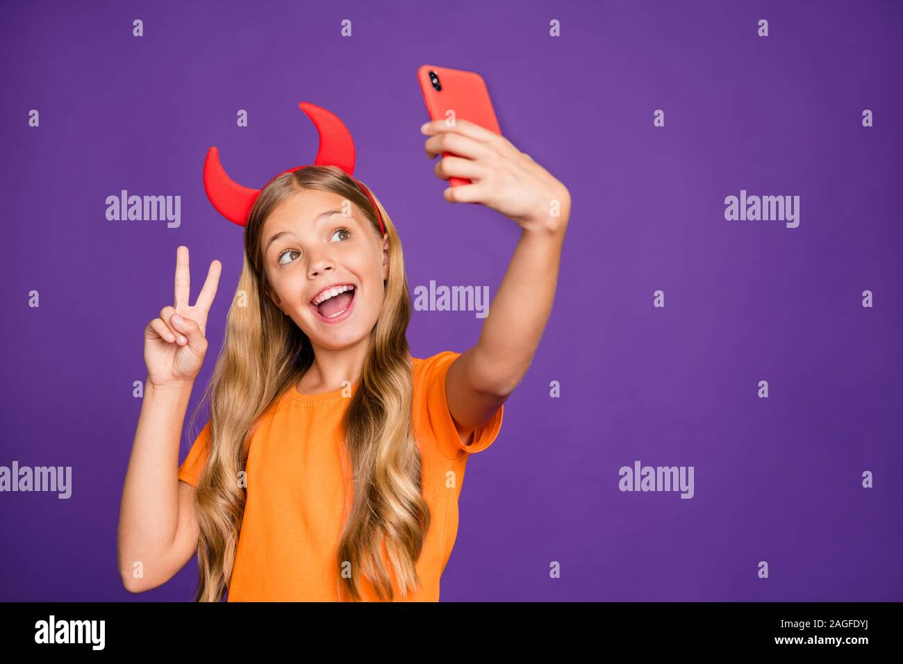 Photo of little lady horns headband holding telephone shooting making funky selfies showing v-sign symbol wear orange t-shirt isolated purple color Stock Photo