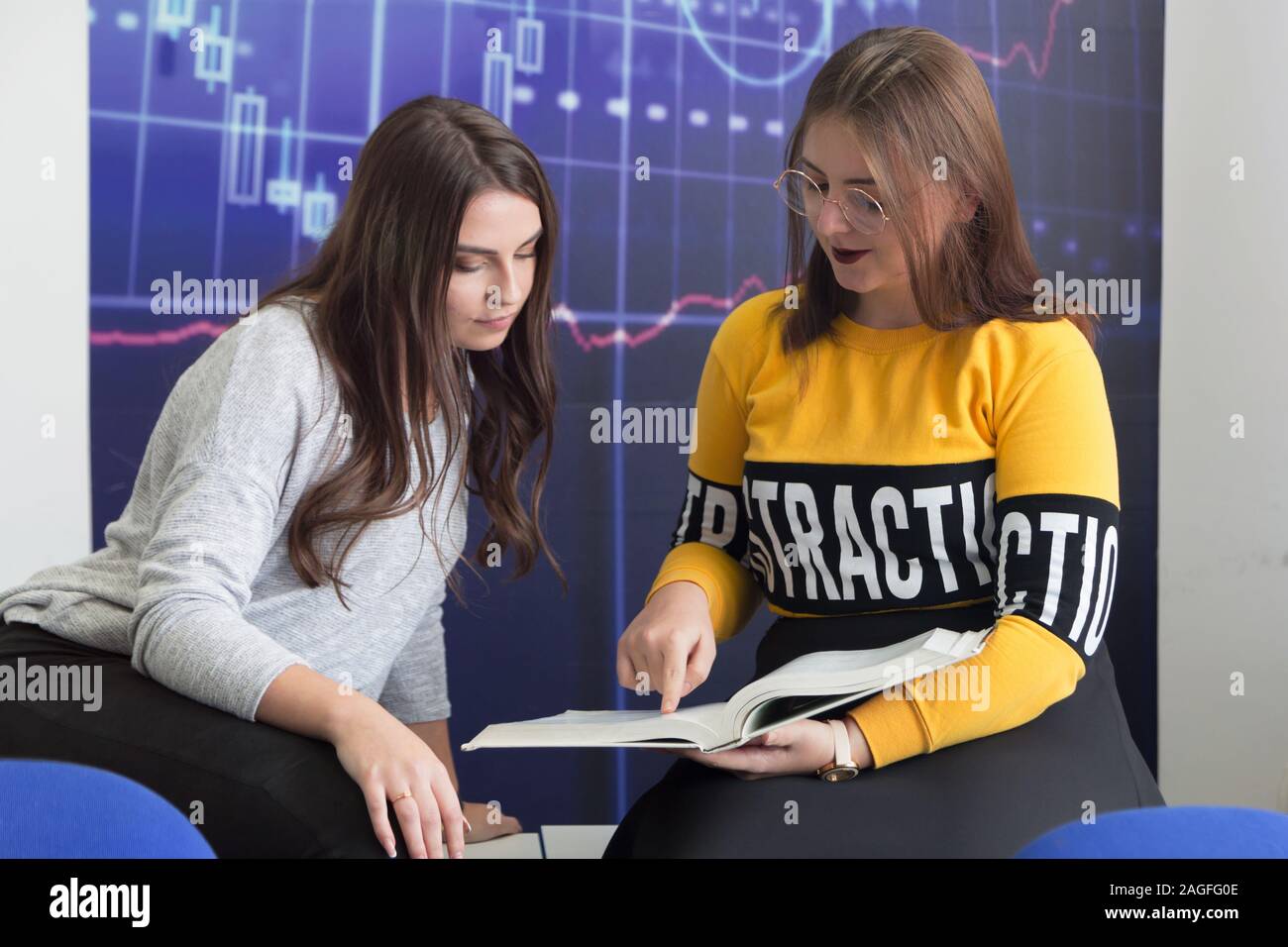 Campus life, students friendship.Two female students helping each other inside classroom. Education, dating, lifestyle concept. Stock Photo