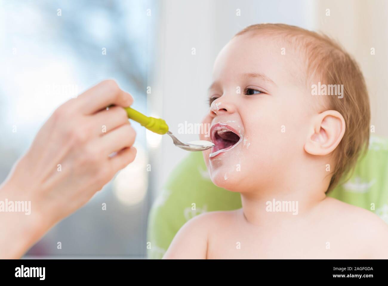 small child sits on a chair and eating with spoon Stock Photo - Alamy