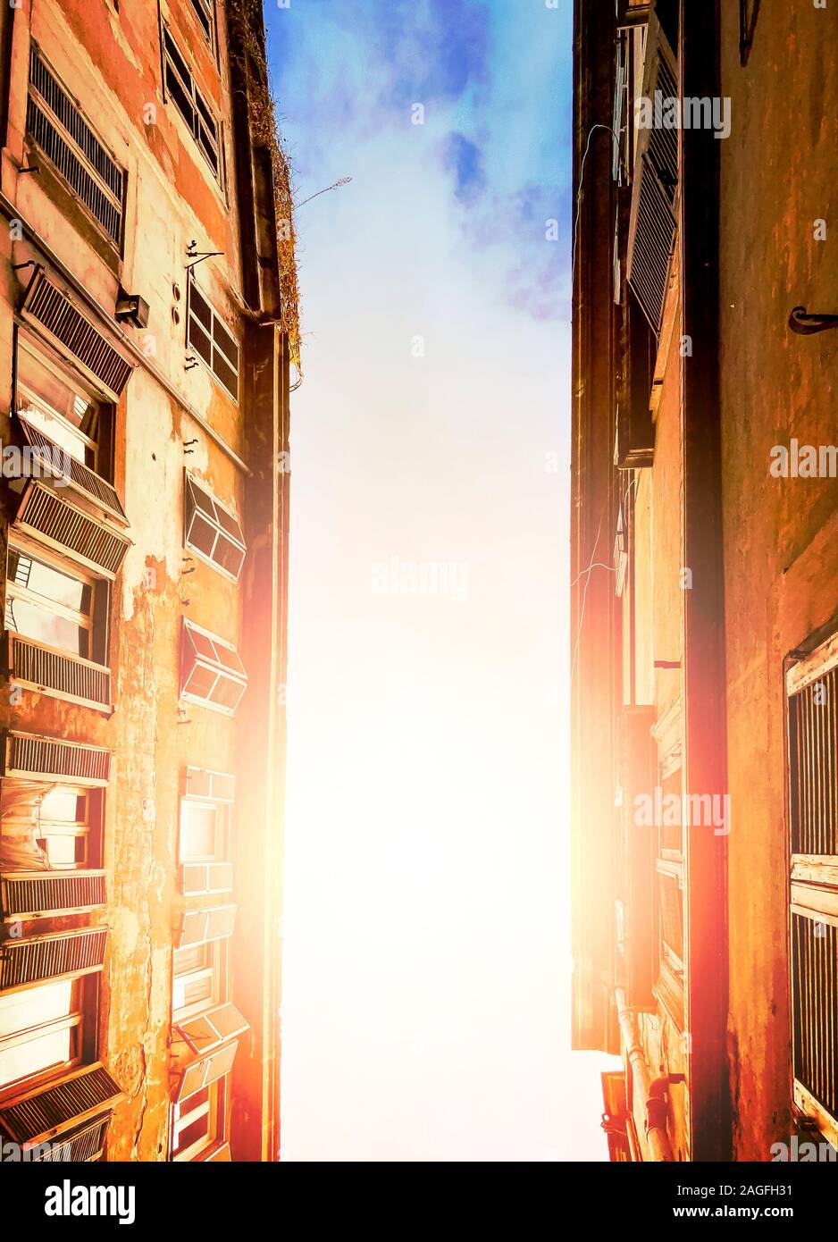 illuminated cloudy sky of the sun seen through the ancient buildings of an alley in Rome during the day. Bottom view with upward perspective. Stock Photo