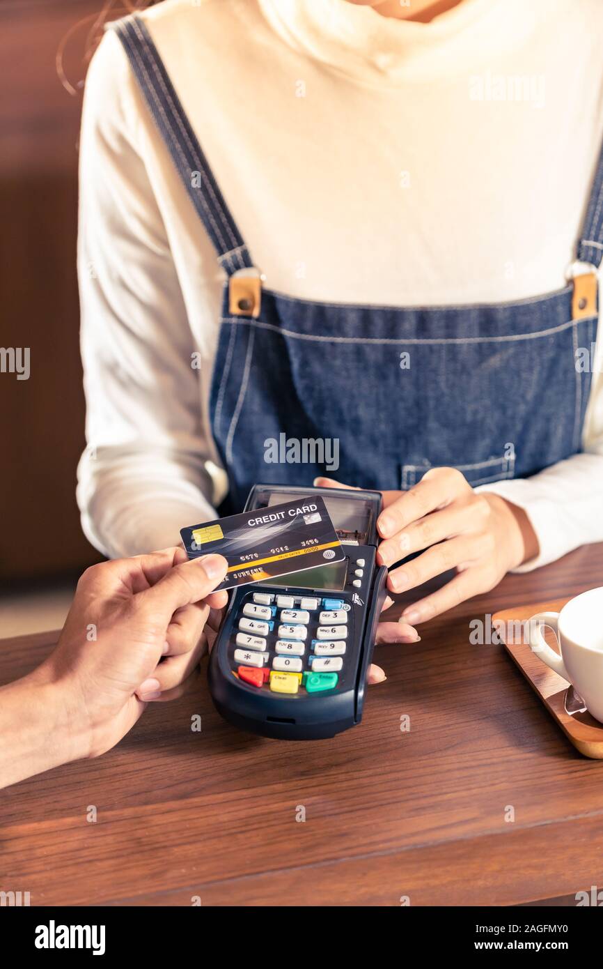 Close-up of asian customer using his credit card with contactless nfs technology to pay a barista for his coffee purchase at a cafe bar. Stock Photo
