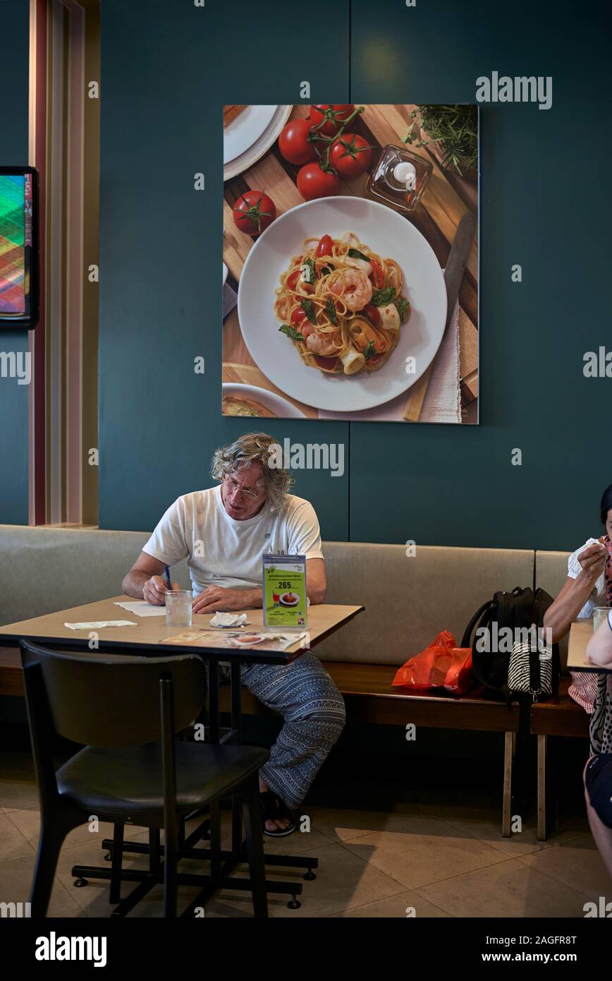 Man alone studying paperwork in a restaurant interior against a wall backdrop of food art Stock Photo