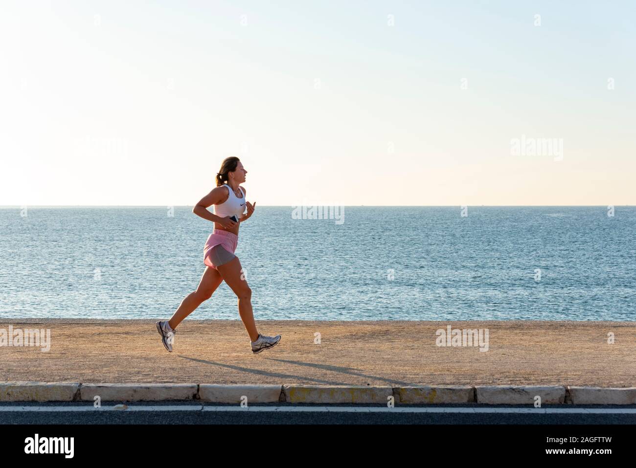 Woman jogging at beach with a phone, Alicante, Spain Stock Photo