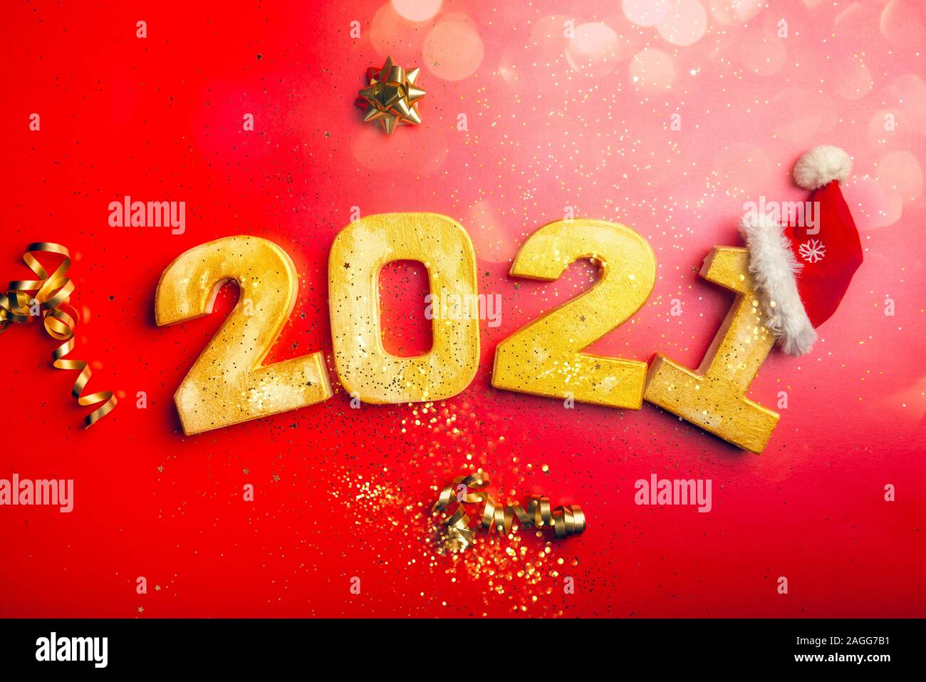 Happy New Year 2021. Golden digits 2021 with christmas hat are on red background with glitter. Holiday Party Decoration or postcard concept with top view and copy space. Stock Photo
