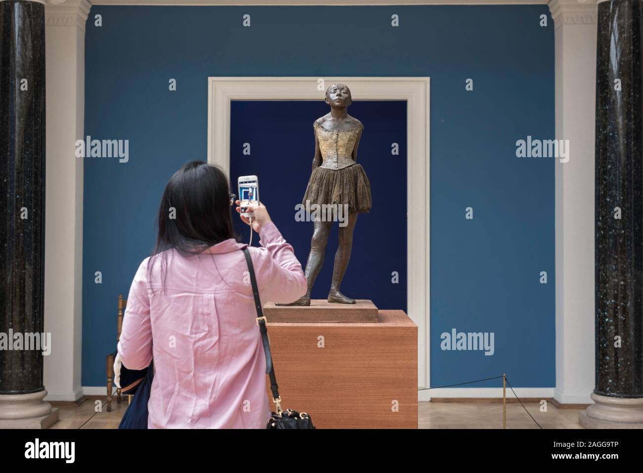 Rear view of  woman photographing the sculpture by Edgar Degas titled The Little 14 Year Old Dancer (1881), Ny Carlsberg Glyptotek museum, Copenhagen. Stock Photo