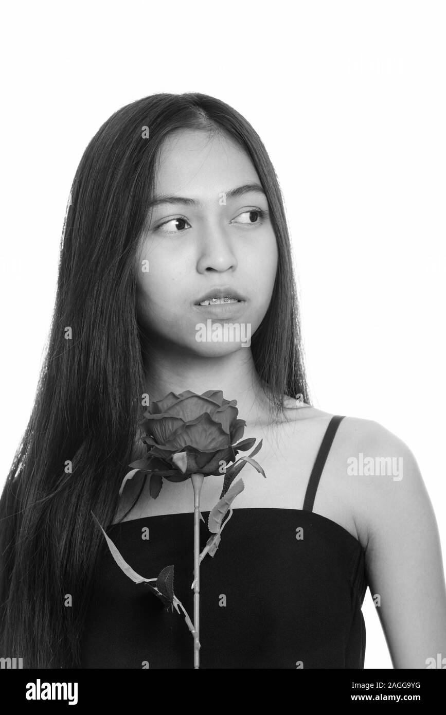 Close up of young Asian teenage girl holding red rose while thinking ...
