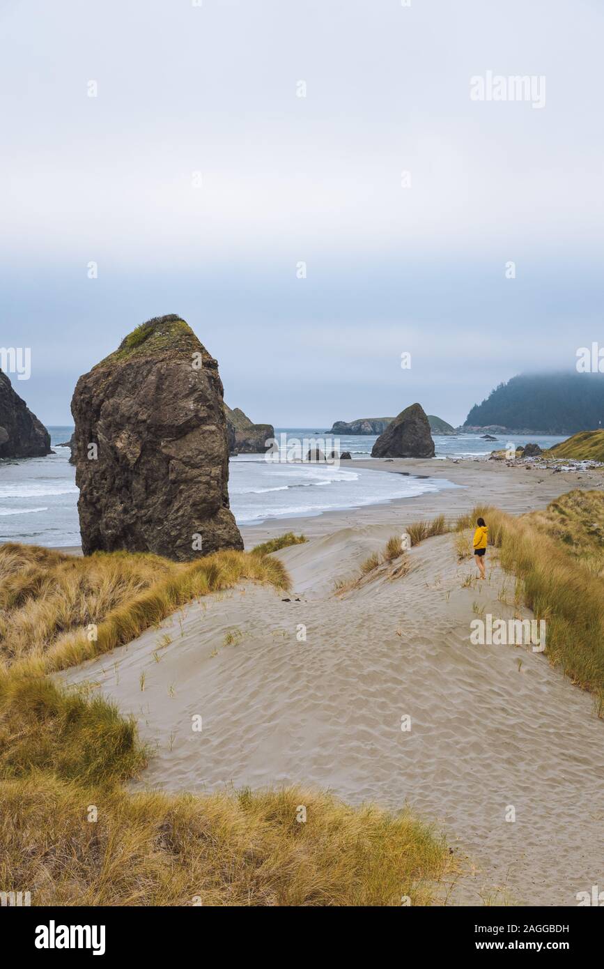 Lone female hiker on rugged coastal beach on moody afternoon, Oregon, USA Stock Photo